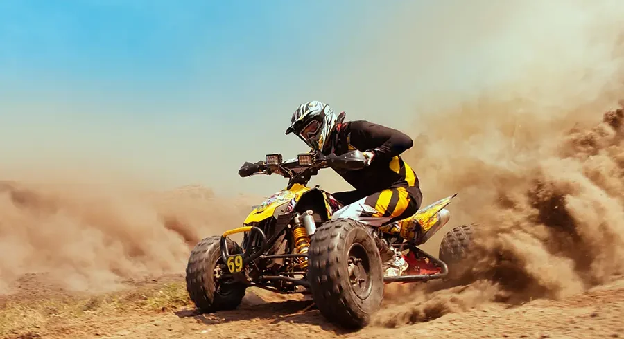 Man on a quad bike racing through desert sand with dust clouds behind
