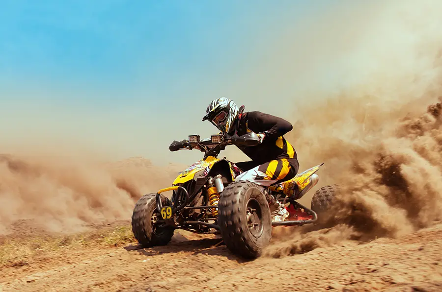 Man on a quad bike racing through desert sand with dust clouds behind